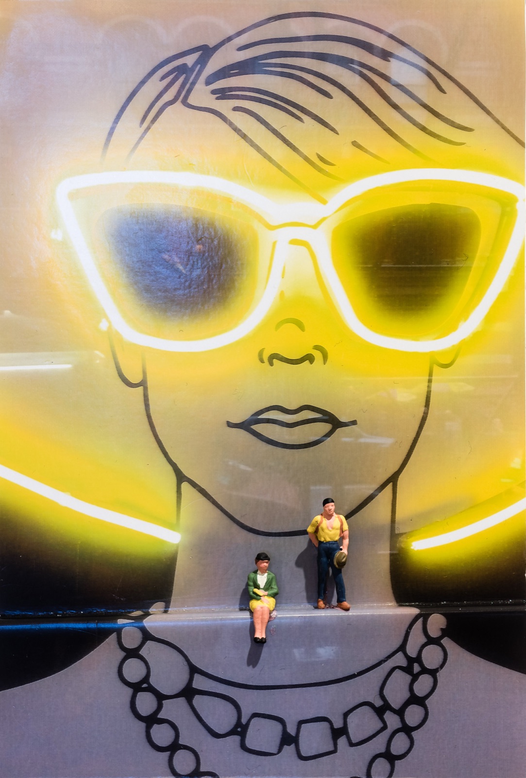 Diorama: Zwei Miniaturfiguren vor einer Neonreklame mit Sonnenbrillen-Motiv